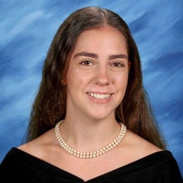 Woman wearing pearl necklace and black dress, smiling at the camera.
