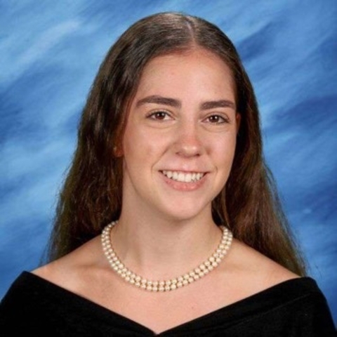 Woman wearing pearl necklace and black dress, smiling at the camera.