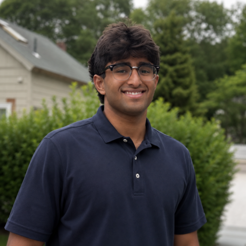Man in glasses smiling in front of green bushes.
